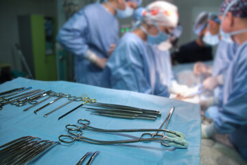 Closeup of surgical tools on table and team of surgery doctors operating a patient in hospital room
