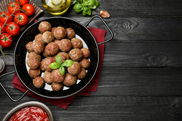 Tasty cooked meatballs with basil on black wooden table, flat lay. Space for text