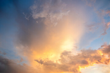 Fototapeta na wymiar Dramatic cloudscape with puffy clouds lit by orange setting sun and blue sky.