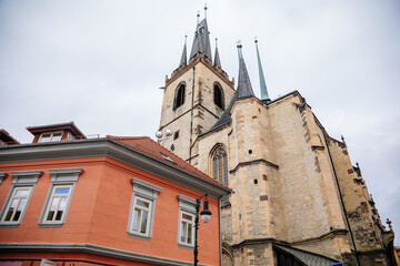 Fototapeta na wymiar Louny, Czech Republic, 19 September 2021: Medieval catholic stone church of St. Nicholas with gothic high spire clock tower in autumn day, Narrow picturesque street in historic city center, arches