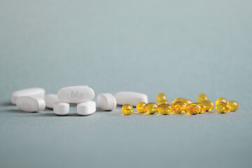 A complex of Mg ( magnesia, magnesium ) and vitamin D ( omega 3 ) capsules for treatment and human health on a light background. Copy space.