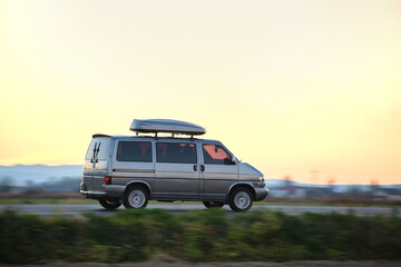 Passenger van with roof rack driving fast on intercity road at sunset. Highway traffic in evening