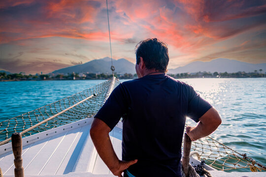 Basilian man watching the sunset on top of a schooner in the city of ubatuba praia itagua in brazil