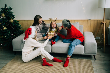 The family celebrate Christmas together. Grandmother, mom and sister give a gift to a little girl. Medium group of people