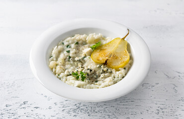 Delicious homemade pear and blue cheese risotto with parsley in white bowl on gray bluebackground