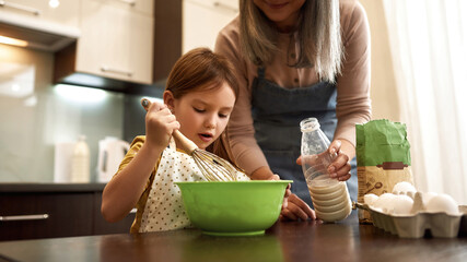 Girl mixing dough in bowl near grandma with milk
