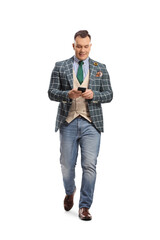 Fototapeta premium Full length portrait of a man in stylish suit and jeans walking and using a smartphone