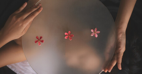 Top view of a woman posing with a round mirror decorated with simple pink flowers