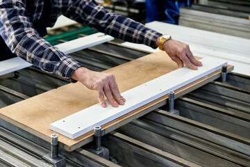 A worker processes furniture blanks on a machine tool in a factory. Industrial production of furniture.