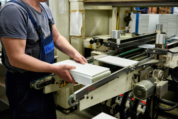 A worker processes furniture blanks on a machine tool in a factory. Industrial production of furniture.
