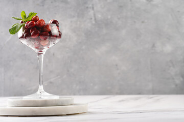 Wide champagne glass filled with fresh raw cranberries on a round marble tray, copy space