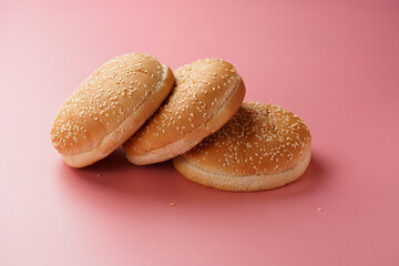 Three white wheat burger buns with sesame seeds on pink seamless surface