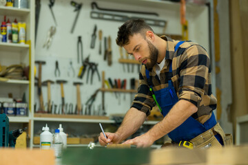 Young caucasian carpenter drawing on board while using angle ruler