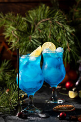 blue cocktail in a tall glass with ice and lemon slices on a wooden background