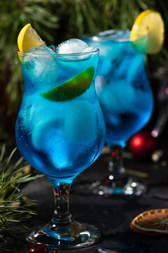 blue cocktail in a tall glass with ice and lemon slices on a wooden background
