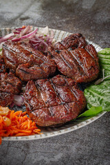 Serving a dish from the restaurant menu. Grilled beef and pork meat with grated carrots and herbs on a plate against a gray stone table, delicious kebab