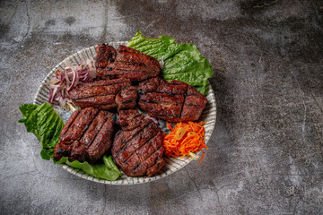 Serving a dish from the restaurant menu. Grilled beef and pork meat with grated carrots and herbs on a plate against a gray stone table, delicious kebab