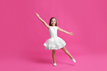 Cute little girl in white dress dancing on pink background