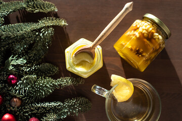 top view of tea with lemon in a cup, Christmas tree twigs and jars of honey on a wooden countertop.