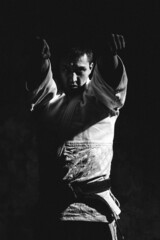 a young man, in a white kimano, shows the elements of karate in the studio on a black background