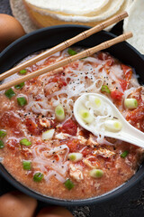 Close-up of tomato egg-drop soup with rice noodles in a cast-iron pan, vertical shot