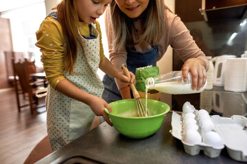 Woman pouring milk in bowl with granddaughter