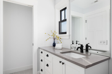 A beautiful white bathroom with cozy decor on the granite counter top, black faucet and window...