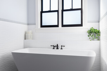 A gorgeous bathroom with a standalone bathtub and black faucet surrounded by wavy, white tile. 