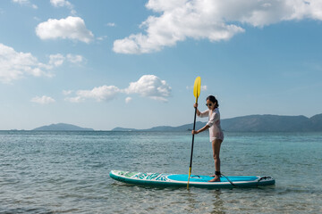 Woman in sunglasses with paddle on sub board floats on ocean.