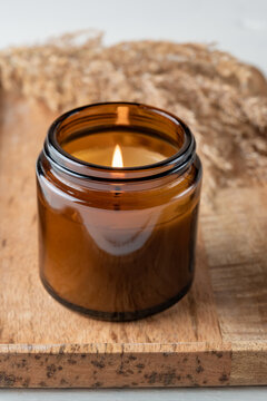Burning aroma candle in a glass jar with the aroma of spices. Autumn atmosphere with dry reeds grass. Cosy lifestyle