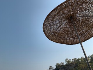 Fototapeta premium Umbrellas on the sandy beach against the background of the sky. Summer theme: relaxation in the sun. A straw umbrella by the sea.