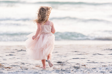 Fototapeta na wymiar A Young Girl Kid Child Dancing Jumping Walking Running in a Pretty Pink Dress Water Sand Sunset Sun Sun light Beach Horizon Fun Get Outside Childhood Unplugged