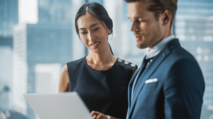 Portrait of Successful Corporate CEO and Investment Manager Talking, Using Laptop Computer while Standing in City Office. Two Successful Businesspeople Brainstorm on e-Commerce Marketing Project.