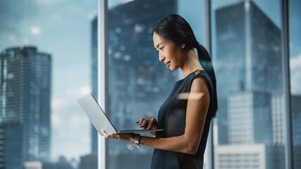 Beautiful Portrait of an Asian Businesswoman in Stylish Black Dress Using Laptop Computer, Posing...