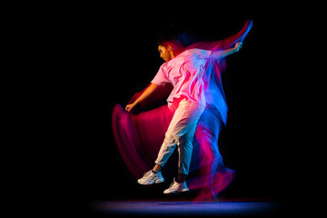 Stylish young girl in white costume dancing hip-hop dance isolated on dark background at dance hall in neon mixed light.