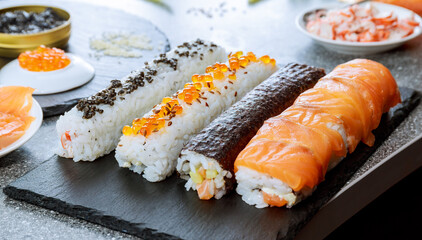 Different types of sushi rolls and ingredients on a black plate. Sushi is widely popular in the world.