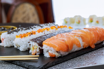 Sushi rolls of various kinds and chopsticks on a black plate.
