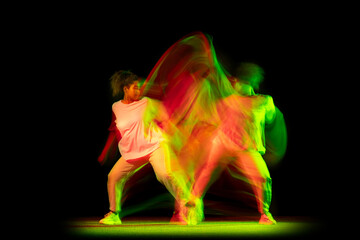 Studio shot of young active girl dancing hip-hop dance isolated on dark background in neon mixed...
