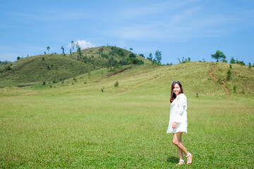 Beautiful Girl stand and acting in front of bald mountain or Phu Khao Ya with green grass field and blue sky. One of natural travel attraction in Ranong province, Thailand