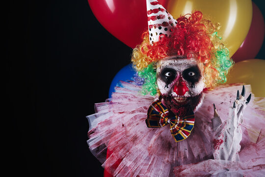 Terrifying clown with air balloons on black background, space for text. Halloween party costume