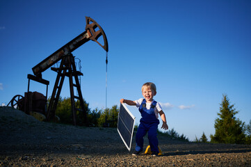 Young kid engineer having fun outdoors in field with oil pump jack at sunny summer day. Smiling...