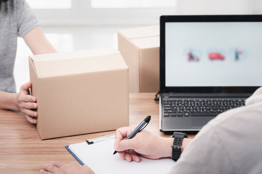 Post man use a pen write on file paper document and check online system to send parcels and women hold paper box laptop on table : delivery concept work
