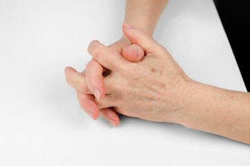 Hands of an elderly woman on a white table, close-up. Folded hands of a woman 60 years old