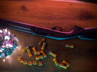 shotgun and cartridges on the wooden table near a christmas tree in cyan and neon light