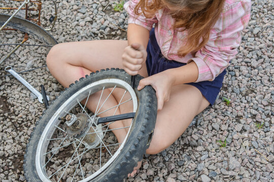 the child girl has damaged a bicycle wheel and is making repairs photo without processing