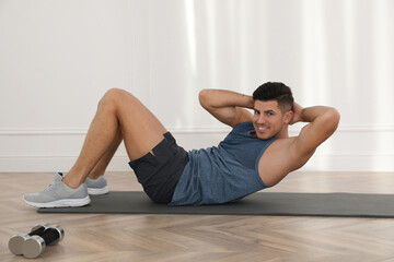 Fototapeta na wymiar Handsome man doing abs exercise on yoga mat indoors