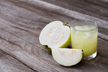 Fresh guava smoothie juice in glass jug and guava fruit with green leaf isolated on wooden table background.