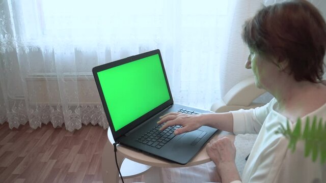 An adult woman with a laptop. An adult woman on the Internet. A laptop with a green chromakey in a woman's hand. Green background