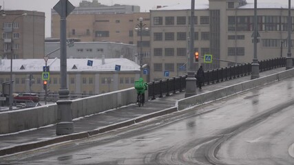 Moscow, Russia - December 2021: Courier by bicycle in winter. A courier on a bicycle delivers in winter during snowfall. Slow motion