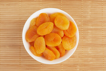 dried apricots in a white plate on a wooden background, top view